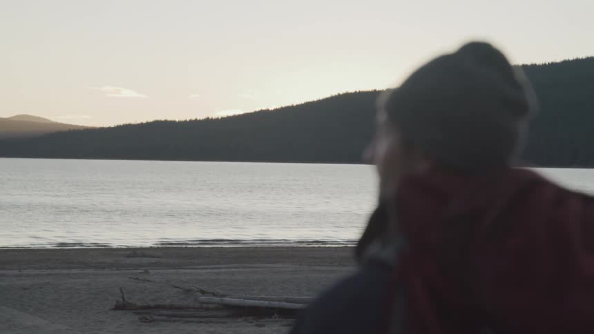 Male hiker stands and watches the smooth lake at dusk