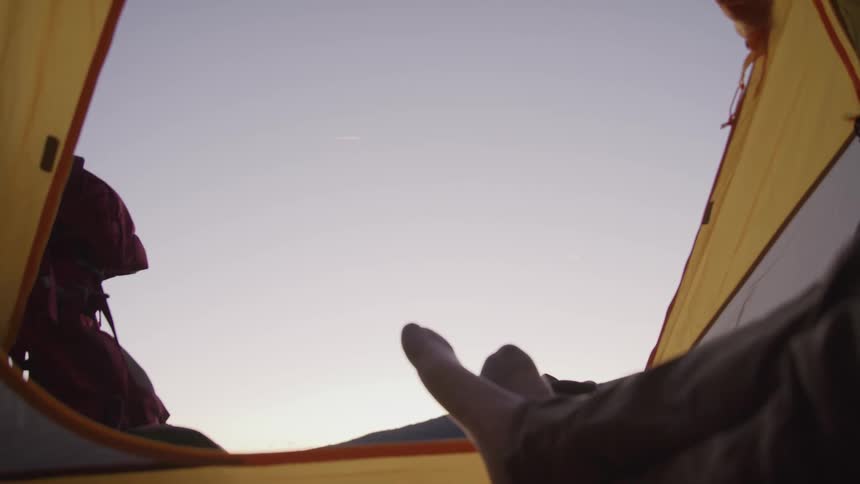 A man sitting in an open tent crosses his legs and looks out to enjoy the view at dusk