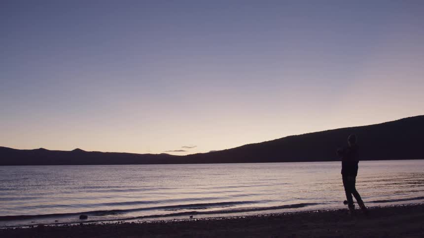A man skips rocks into a lake at sunset