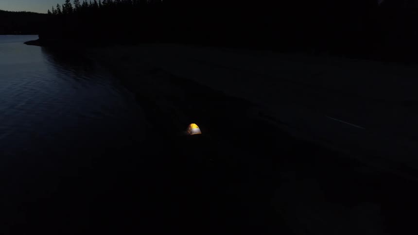 The tent is lit inside near the lake