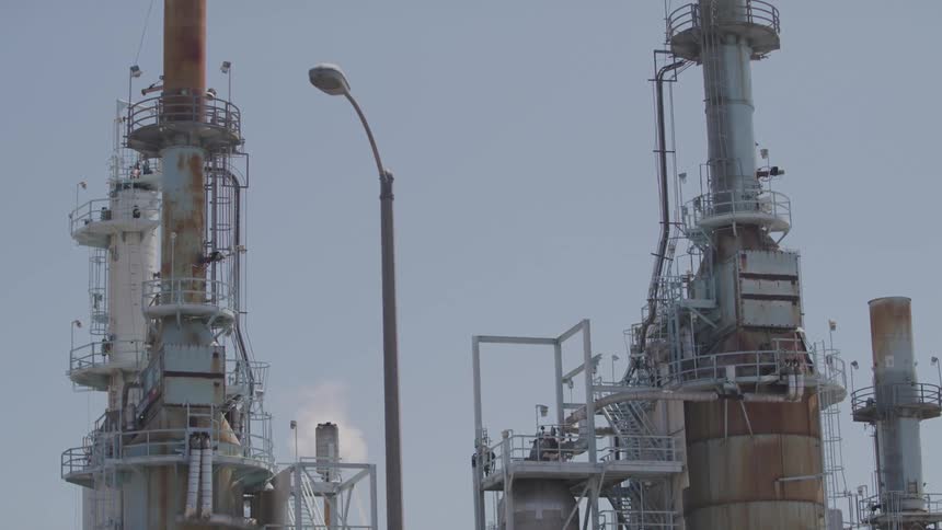 The towers of a factory standing high over a road as traffic passes by