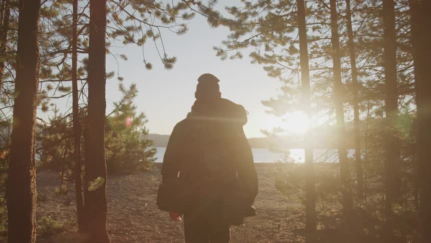 Man walking out of the woods towards a lake