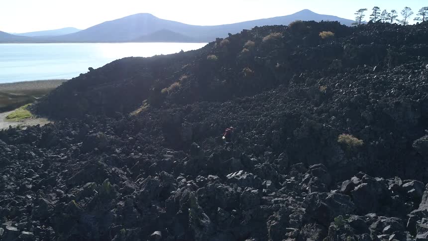 A person walks across rocks in front of a lake