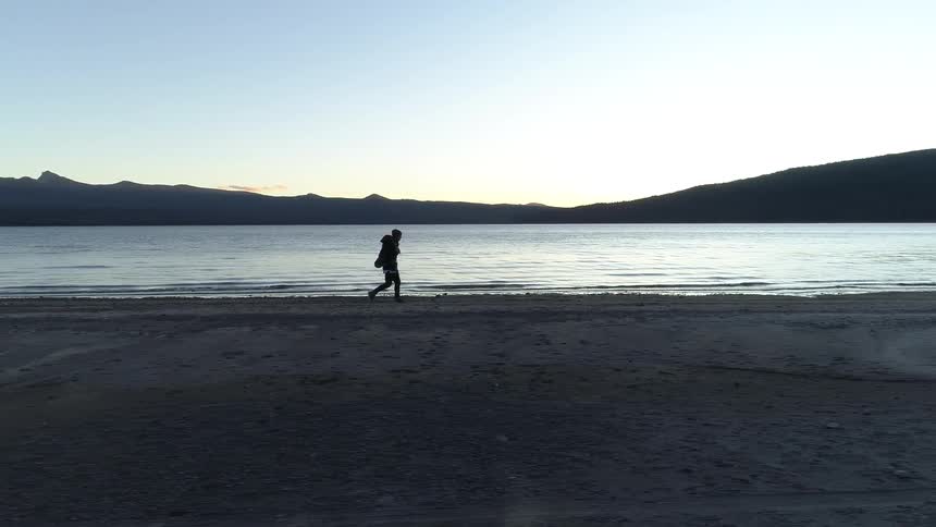 Backpacker walking along the shoreline near a lake at dusk