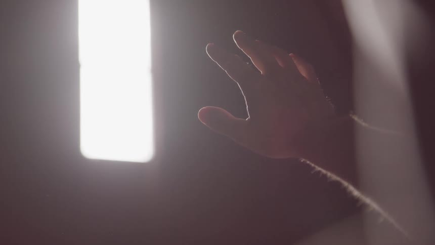 Hand reaches towards a bright window