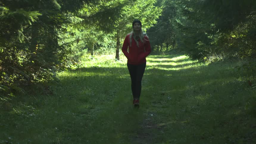 Blonde woman walks along the forest track in the woods