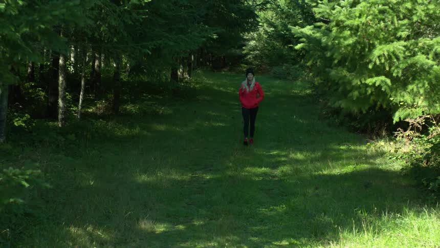 Woman walking through the forest on a grassy trail