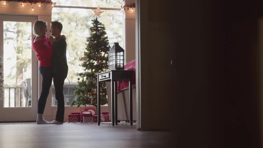 Man and woman dance and kiss each other near the christmas tree in the living room at home
