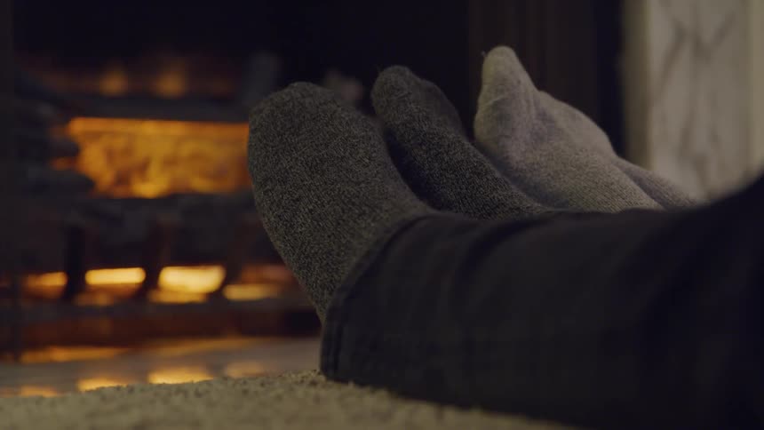 Two people rub feet together by the fireplace