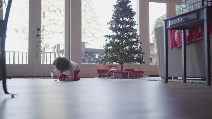 Black child sitting on the floor writes a letter to santo in the living room