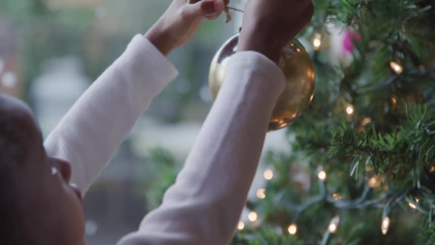 Black girl putting ornaments into a christmas tree