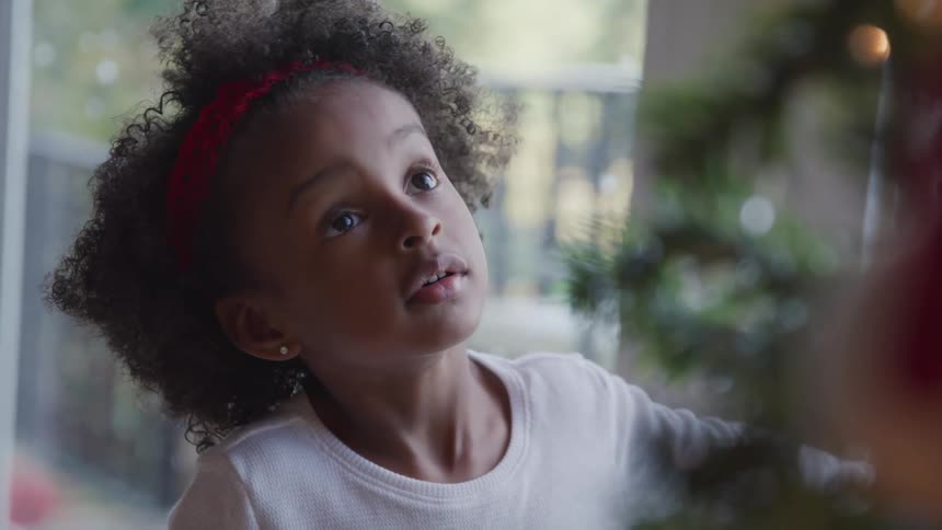 Black little girl looks up at the christmas tree in the living room at home