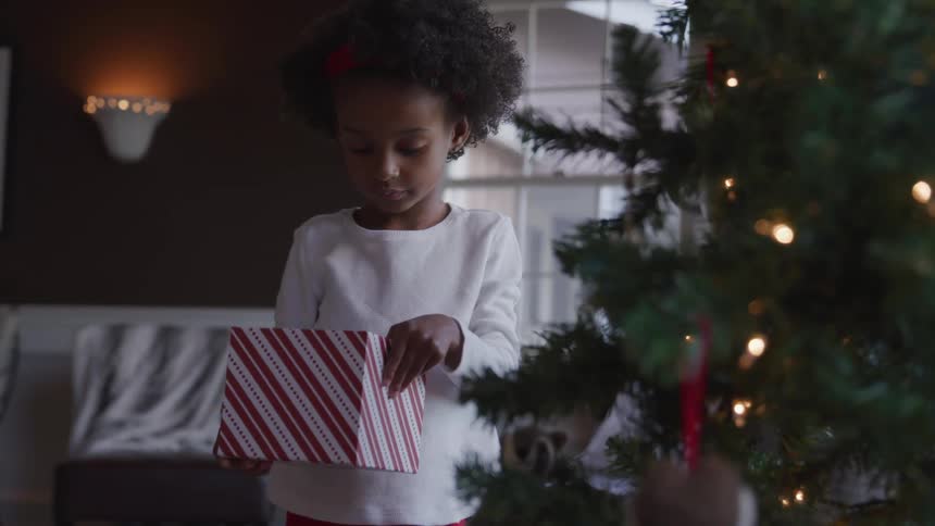 Black child stands and holds a gift box near the christmas tree