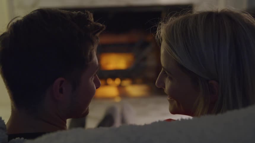 White couple romantically sitting together at the couch in front of the fireplace