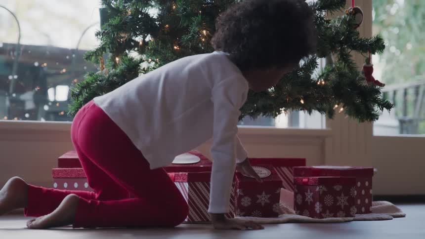 Black child touches the gift box under the christmas tree in the living room at home