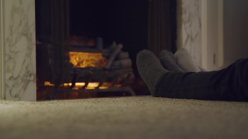 Man and woman sitting on the floor warm their feet in front of the fireplace in the living room at home