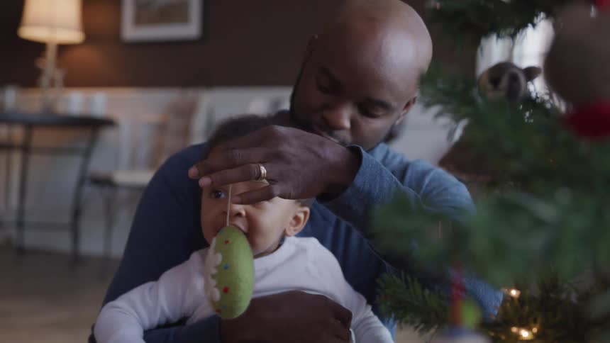 A dad sitting on the floor holding his child and playing with an ornament