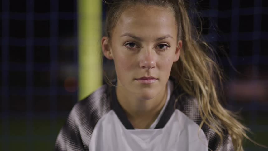 A soccer player poses in front of a net at night