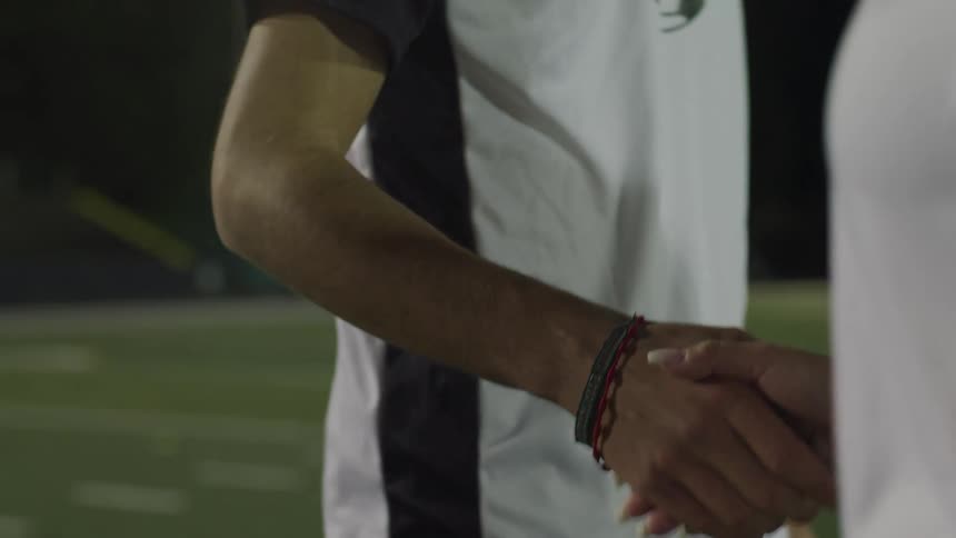 A male and female athlete shake hands on the field
