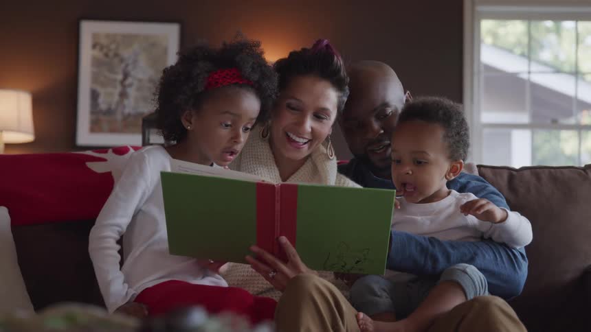 A family sits on the couch and the mother reads to the two children