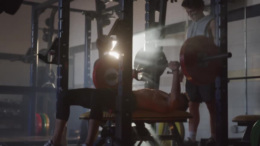 A teenager lifts weights as two others encourage and cheer him on
