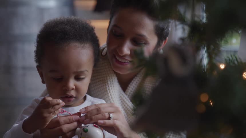 Mother and toddler daughter decorate the christmas tree with christmas bulb in the living room at home