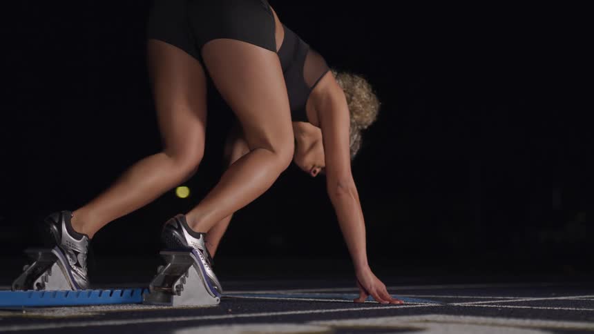 A woman crouching down in the starting line of a running track then begins to run