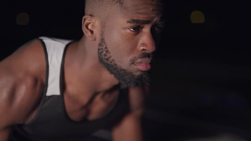 Man in tank top crouches down outdoors at night
