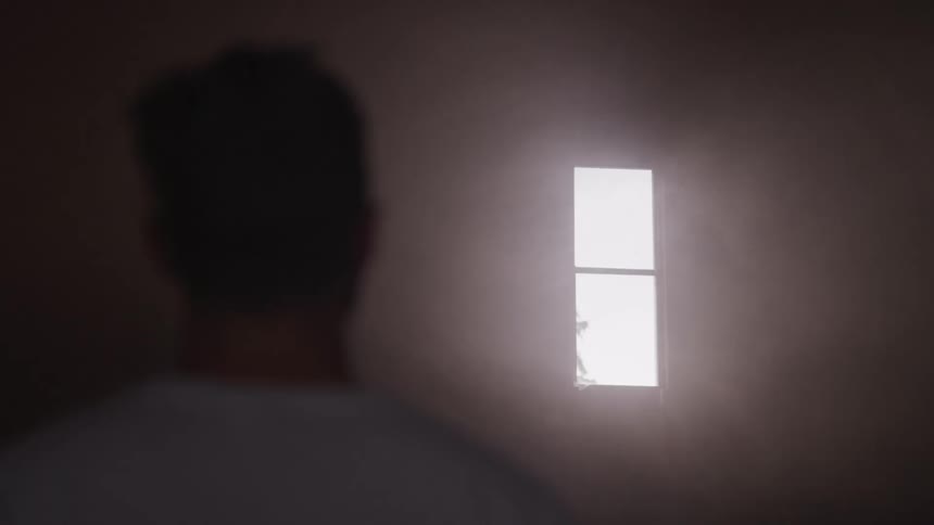 Man stands in building looking up toward light coming in through window