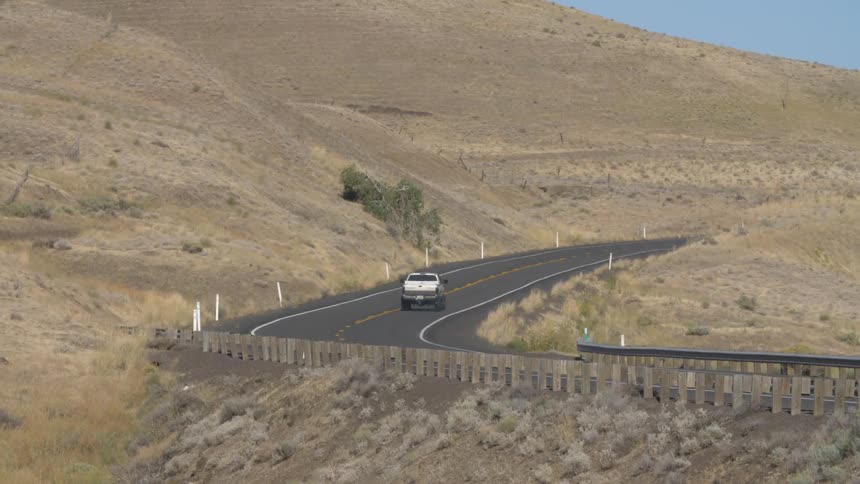 A truck traveling along a road at the base of a tall set of hills