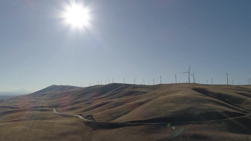 Sun shines high in the sky over wind farm occupying top of hill