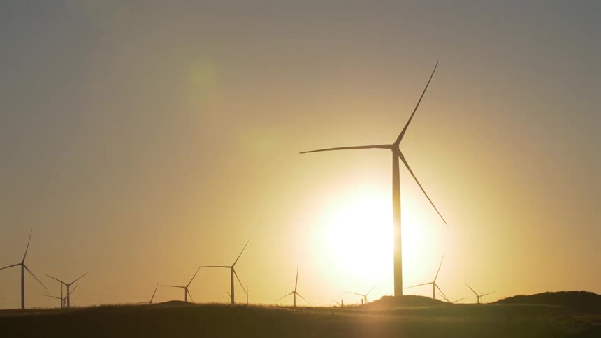 A wind turbine farm with the sun in the background
