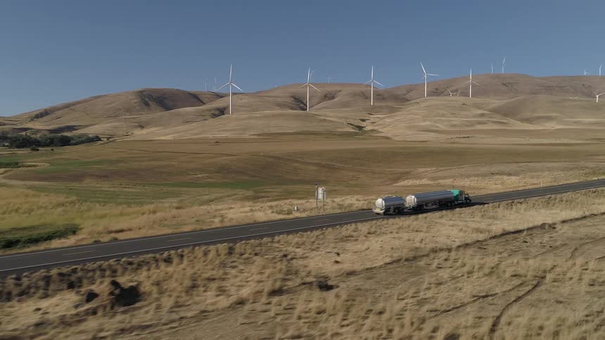 A tanker truck drives down a rural two lane road past wind turbines