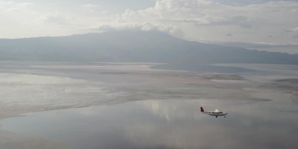 A plane flies over water on a cloudy day
