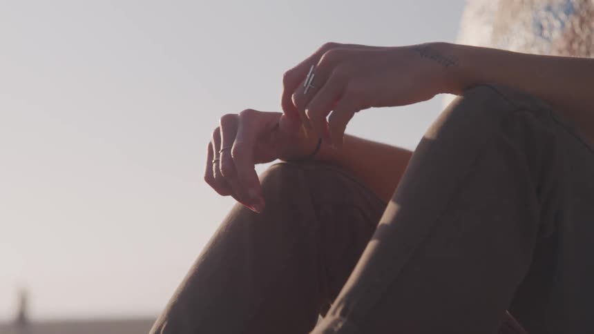A man sits against a large rock on the beach with his knees to his chest