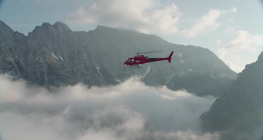 A helicopter flying near mountains over the clouds with the sky in the background