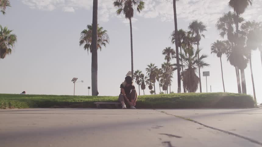 A female skateboarder sitting down to tie her shoes and rest for a moment before rising and skating out of frame