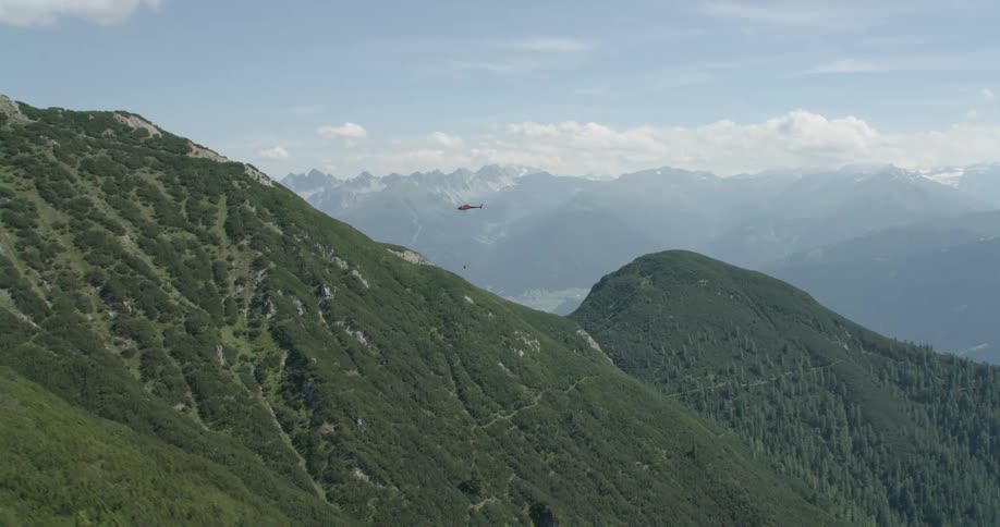 A red helicopter flies over a mountain