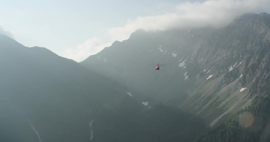 Aerial shot of mountains reaching the clouds with a helicopter flying in between