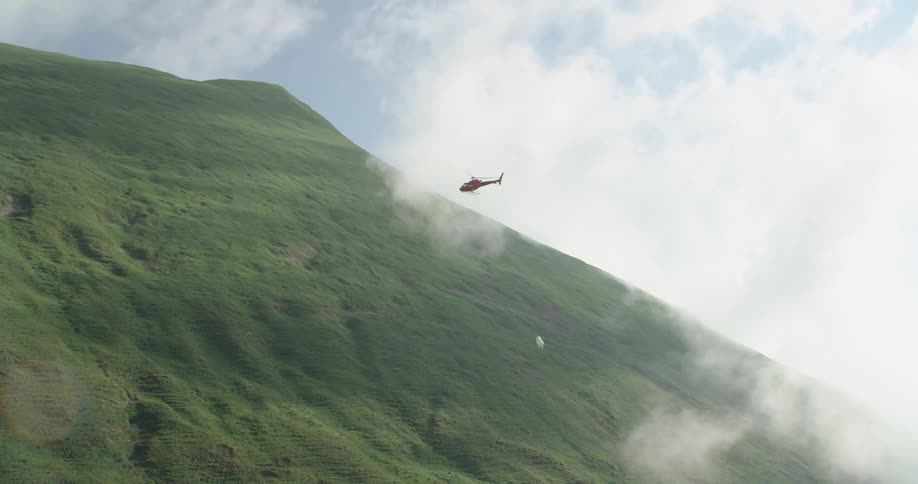 A helicopter flying toting a load with the sky in the background