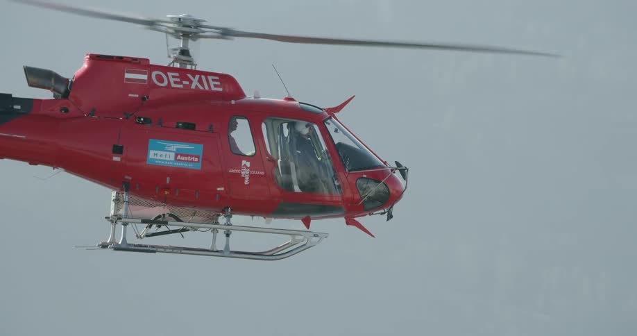 A red emergency firefighting helicopter flies along a smoky ridge