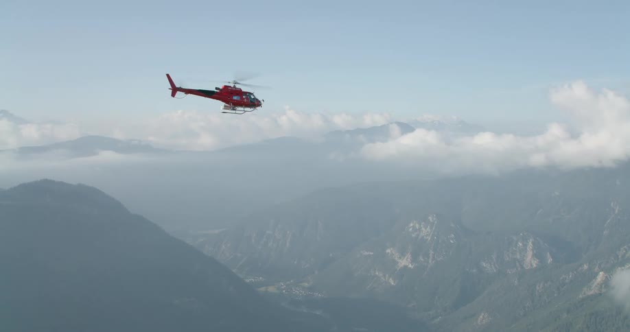 Red helicopter flies forward and backward over mountain valley
