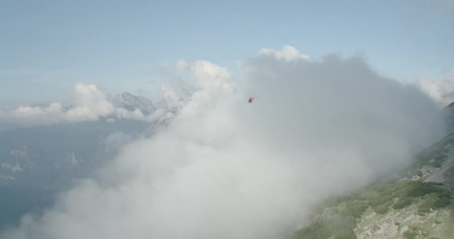A helicopter flying near clouds and mountains