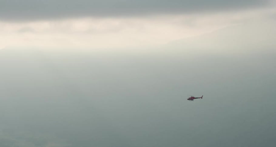 Helicopter far away flying close to the clouds
