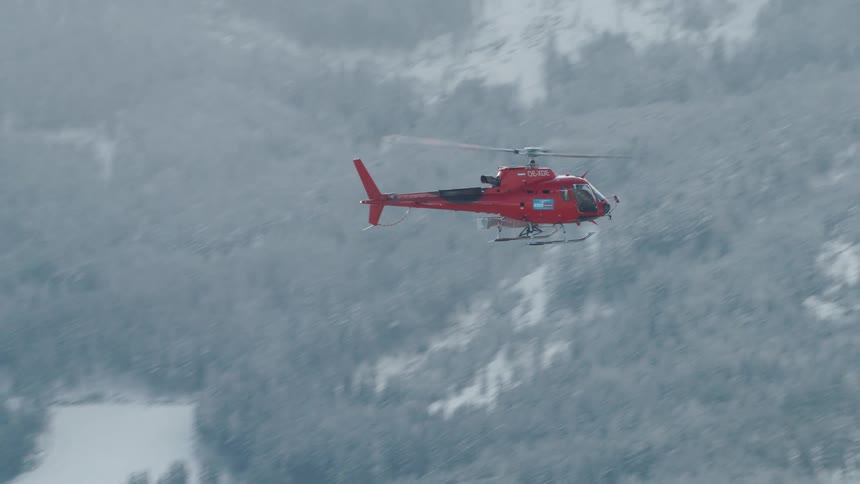 A helicopter flies over a forest area with smoke surrounding