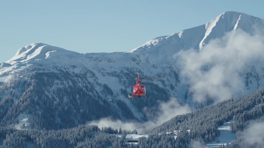 Red helicopter increases altitude near the snowy mountains