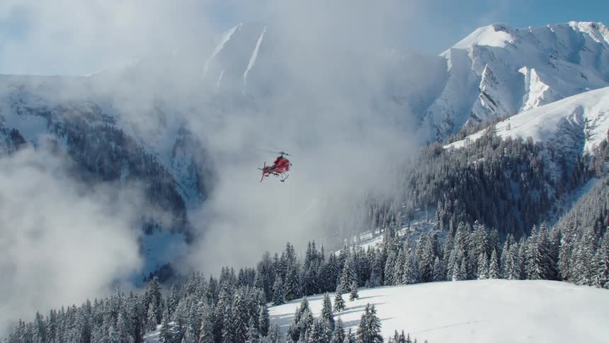 A helicopter flies over snow covered mountains