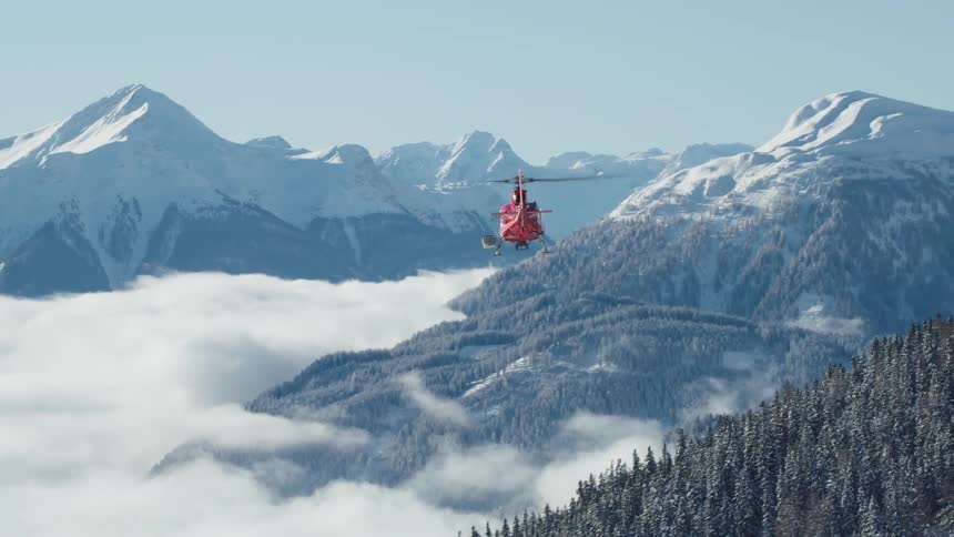 Search and rescue helicopter flies over the snow capped mountains