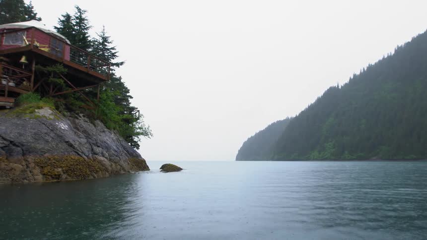 Rain falling over a cabin in a lake surrounded by mountains