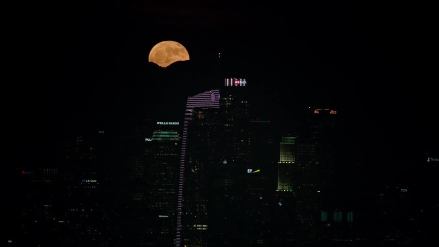 Super moon rises behind mountain range behind city skyline at night